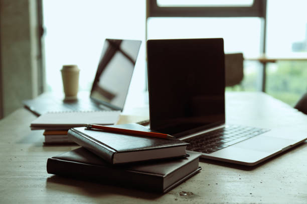 A laptop with documents, notebooks and a cup of coffee on the table