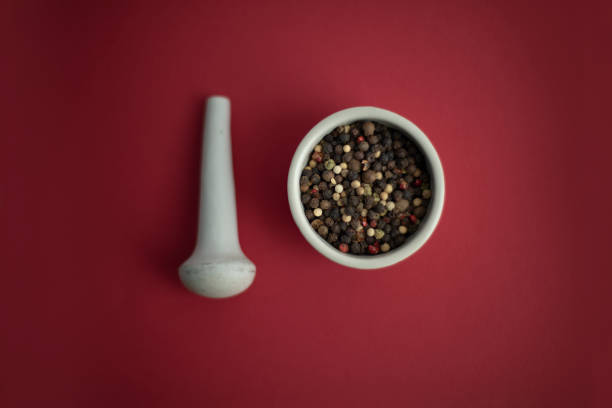 Ceramic mortar and pestle with peppercorns on red background. Black pepper and bay leaf in a white bowl on a red background