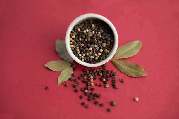 Ceramic mortar and pestle with peppercorns on red background. Black pepper and bay leaf in a white bowl on a red background