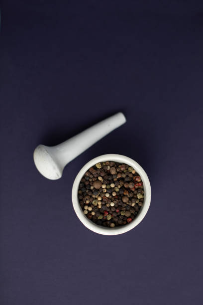 White mortar and pestle with peppercorns on a blue background