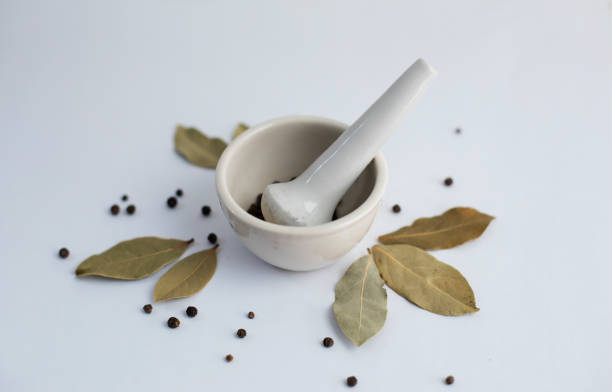 White mortar with black pepper and bay leaves on a white background.