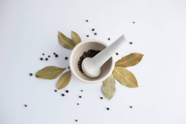 White mortar with black pepper and bay leaves on a white background.