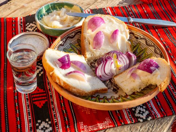 Traditional Bulgarian breakfast with bread, lard, and red onions on a colorful tablecloth, accompanied by a glass of water.