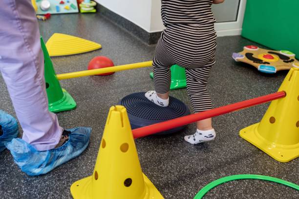 A toddler in striped clothes playing on a colorful balance course with cones and bars indoors.