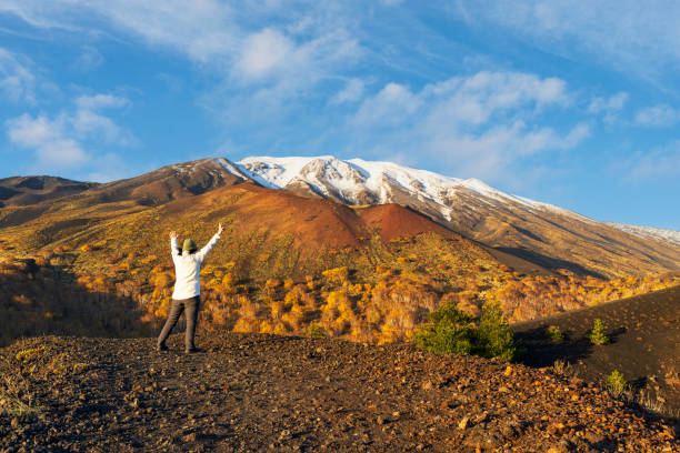 Rear view of a female hiker with arms outstretched admiring Mount Etna covered with snow in autumn, UNESCO world heritage site, Sicily, South of Italy, Italy, Europe