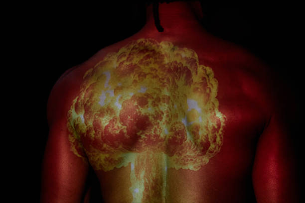 Cropped shot of strong back of man standing in projector light displaying image of nuclear bomb explosion against black background, copy space