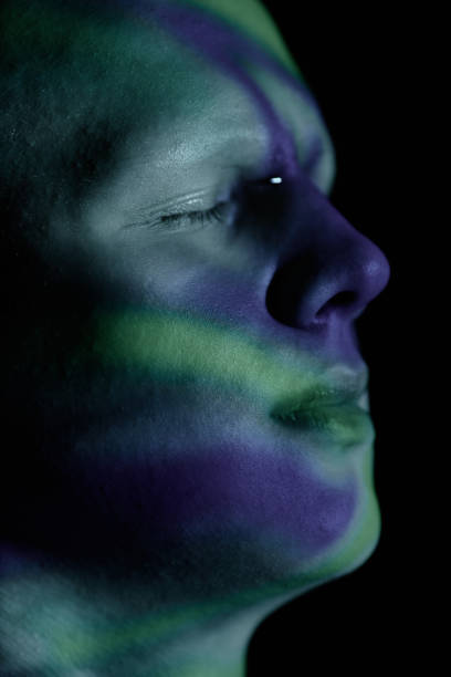 Extreme close up of man with eyes closed drown in thoughts with blue and green lights projecting onto relaxed face against black background in studio