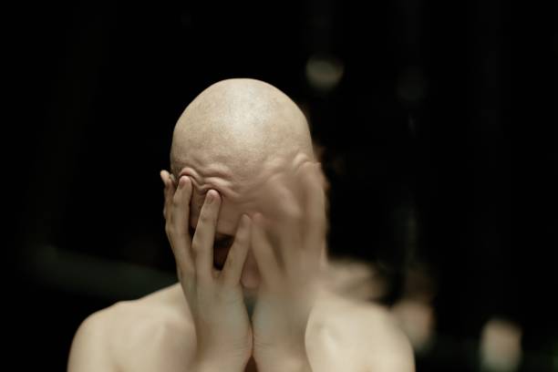 Distorted by water image of pale bald man covering face with hands in feeling of despair drowning in gloomy thoughts against black background in dimly lit studio, copy space