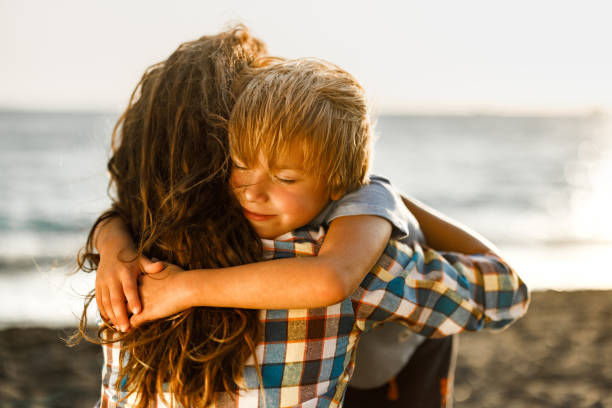 istock Loving little boy embracing his single mother on the beach. 2193086807