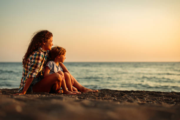 Happy single mother and son relaxing on the beach at sunset.