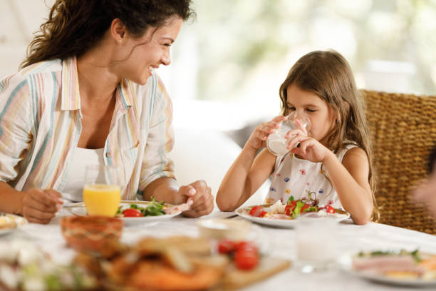 istock Little daughter drinking milk during breakfast with her mother at home. 2193088611