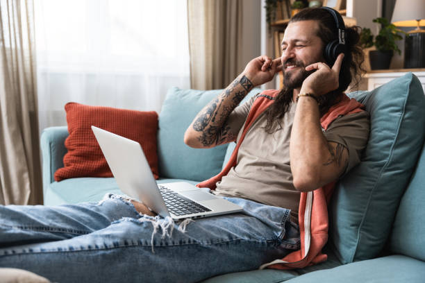 istock Young man working from home, doing IT work from his home on laptop computer and listening to music on his wireless headphones. Music expert and blogger blogging about new albums or songs on his blog. 2193090923