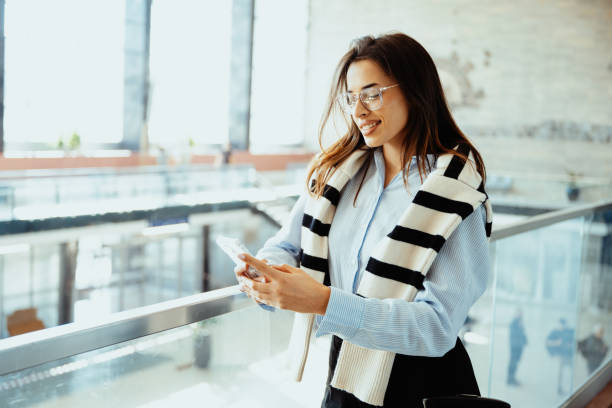 istock Smiling young woman using smartphone in modern bright office building while wearing casual stylish outfit and glasses 2193092787