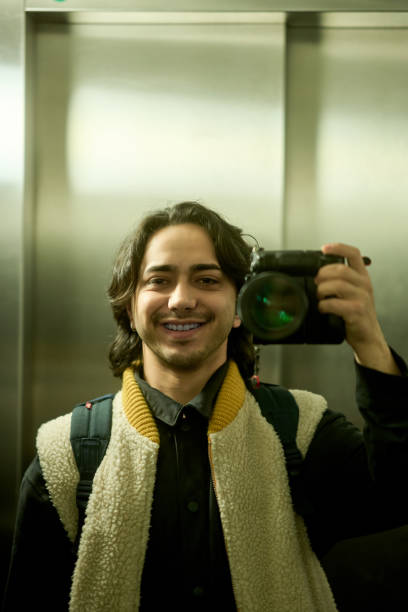istock Young photographer smiling and holding camera in elevator 2193095169
