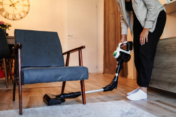 A view of a person tidying up a cozy living area using a stylish cordless vacuum cleaner. The neatly arranged furniture and decor create a comfortable ambiance of a modern home environment.