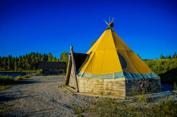 A teepee is sitting in a field with a blue sky in the background. The teepee is yellow and has a conical shape
