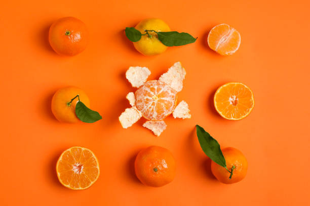 istock Delicious tangerines and green leaves on orange background, flat lay 2193108974