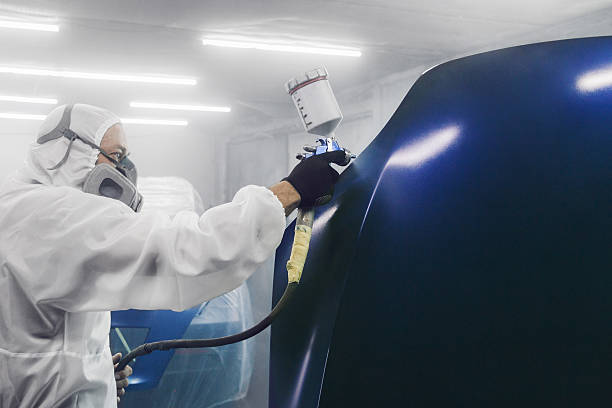 istock Professional bodywork, male car painter in protective mask and workwear apply few layer paint from spray gun to automobile body parts in garage booth. 2193109192