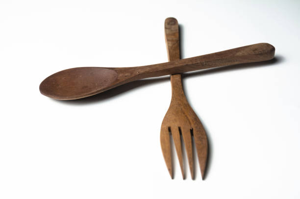 Close-up stock image of rustic wooden kitchen utensils, including spoons and forks, placed neatly on a clean white isolated background. This image highlights the natural texture and warm tones of wooden cutlery, perfect for use in cooking, dining, or kitchen-related themes. Ideal for product photography, culinary blog posts, and lifestyle websites. The simple yet elegant composition emphasizes the timeless charm of wooden kitchen utensils, offering versatility for various creative projects.