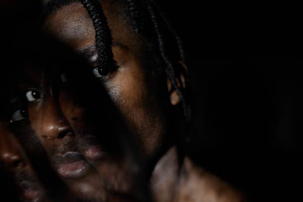istock Portrait of Black man Staring at Camera Hiding Face in Shadows Posing in Dark Studio 2193114620