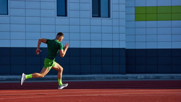 istock Dynamic photo of runner in green speeds down track, his powerful stride emphasized by sunlit against modern building backdrop. 2193117013