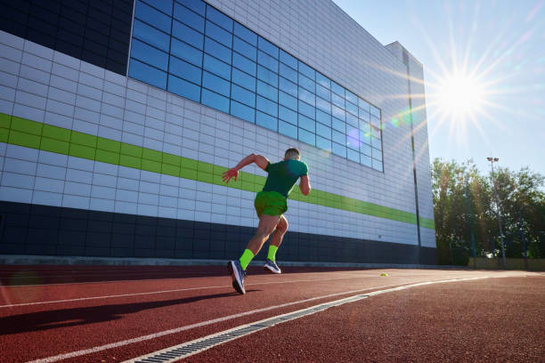 istock Focused and fast, athlete in green races along track, with the sleek building facade adding modern touch to his sprint. 2193117029