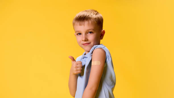 istock Little boy posing demonstrating patch on hand and gesturing thumb up after vaccination against yellow background. 2193117130