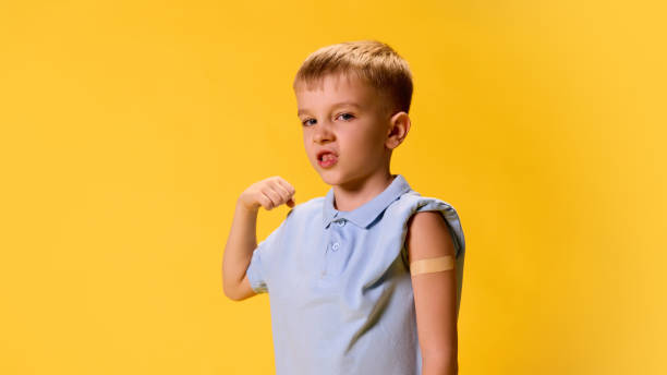 istock Little, confident boy posing shows his muscles and demonstrate arm with patch after vaccination against yellow background. 2193117135