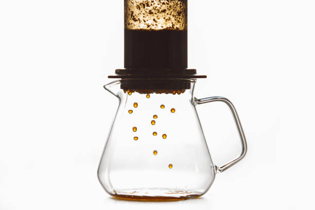 Close up isolated shot of skilled barista brewing coffee by creates pressure known is aeropress method where drops flow from flask into glass pot, creating rich and fragrant coffee drink against white background with a free copy space. Concept of alternative coffee making.