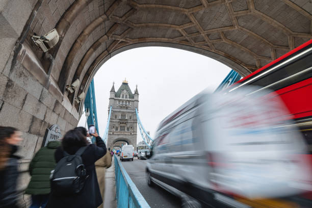 A Hispanic tourist takes a photo of the famous Tower Bridge in London. The bustling scene includes vehicles crossing the bridge, capturing the essence of travel and exploration in this iconic city. Joy and adventure are in the air.