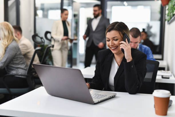 istock Positive Woman Typing on Laptop and Talking on Telephone Multi-tasking in Office 2193122012