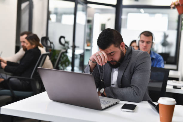 istock Male Employee Looking Exhausted at Office Leaning His Head on Hand Looking Down 2193122092