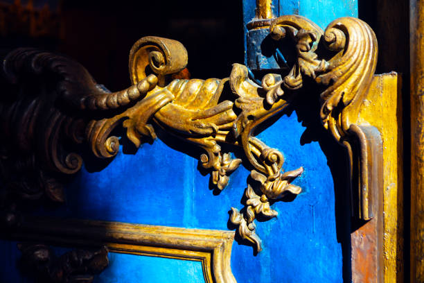 Intricate golden baroque ornamentation set against vibrant blue wooden surface, illuminated by dramatic lighting that emphasizes its curves and details. Golden carvings against vibrant blue background