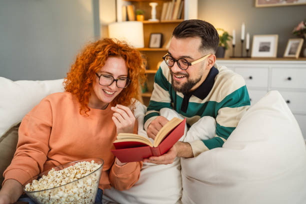 istock cheerful couple enjoy together on sofa with book and popcorn 2193124786