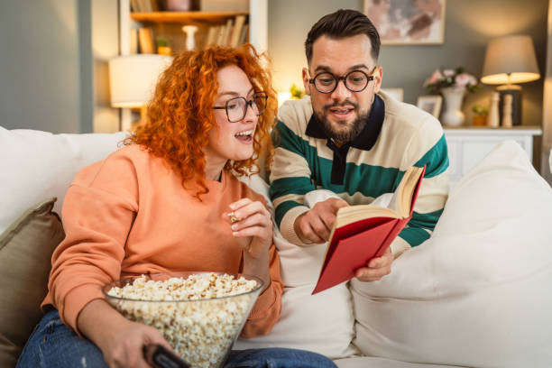 istock cheerful couple enjoy together on sofa with book and popcorn 2193125529