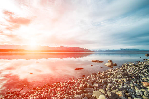 Sunset at Mount Cook National Park alongside Lake Pukaki with snow capped Southern Alps basking in the late winter afternoon's golden light. The setting sun cast vivid pastel hues on the sky.