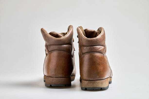 Pair of worn old yellow hiking trekking lace boots Isolated on white glossy surface with beautiful reflection effect. Second hand tourist walking shoes. Back view. Copy Space. White background.