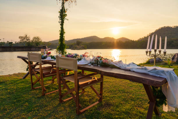Rustic and romantic elegant outdoor dining setup with wooden long table, chairs, tableware, cutlery, candle and flora decoration in the sunset