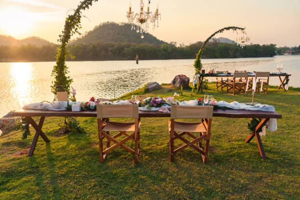 Rustic and romantic elegant outdoor dining setup with wooden long table, chairs, tableware, cutlery, candle and flora decoration in the sunset