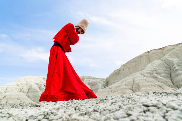 Beautiful young girl in a red dress sits on a stone in the park