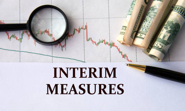 istock INTERIM MEASURES - words on a white sheet against the background of a chart, magnifying glass and banknotes 2193136114