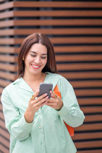 istock Urban woman smiling brightly while texting, modern architecture and wooden textures complement her green shirt 2193138779