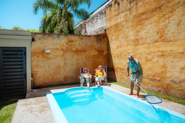 istock Elderly Couple Relaxing by a Backyard Pool with Man Cleaning Water 2193140561