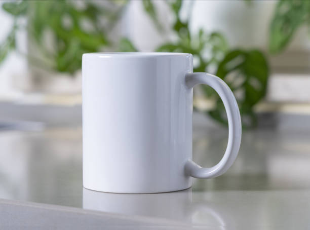 istock White coffee mug on grey kitchen table against green plant closeup, mockup 2193140753