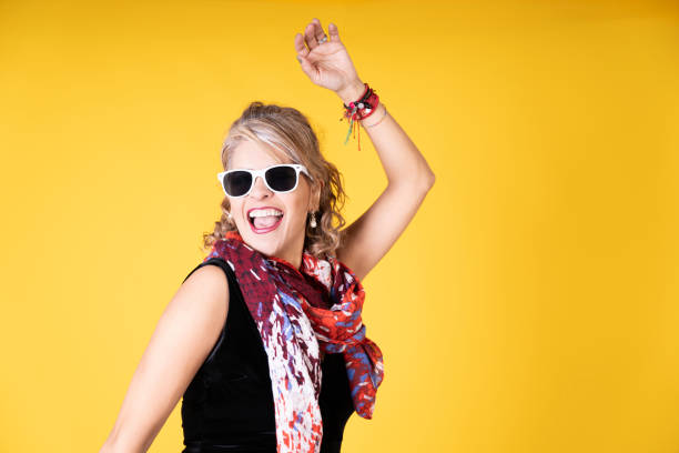 Portrait of a stylish mature woman dancing and enjoying herself on a vibrant yellow background