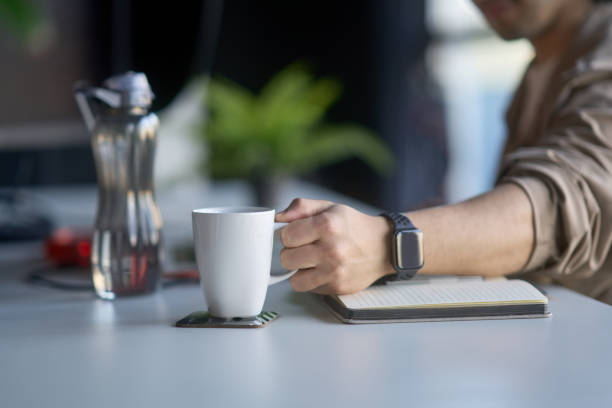 Office worker holding coffee mug and notebook at desk