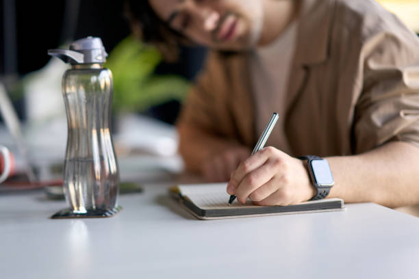 istock Young adult man writing notes in notebook at office desk 2193150329