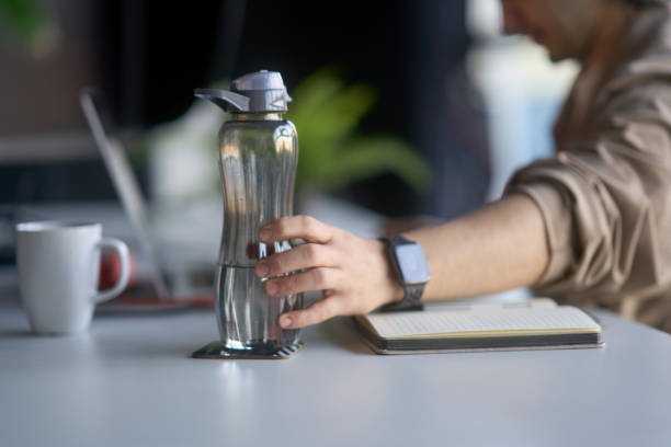 istock Office worker grabbing reusable water bottle at desk 2193150351