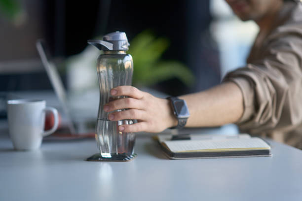 istock Office worker grabbing reusable water bottle at desk 2193150352