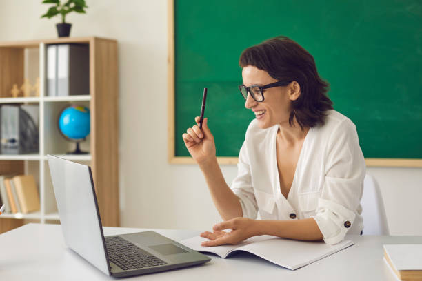 istock Happy school teacher sitting at desk with laptop and having virtual class with students 2193150579